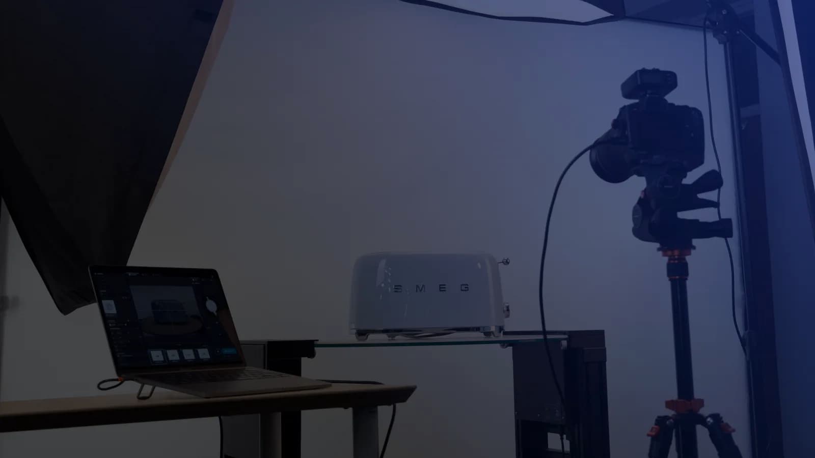Set de fotografía de producto con tethering: un notebook con el software de captura junto a una cámara en trípode y un producto sobre una repisa de vidrio