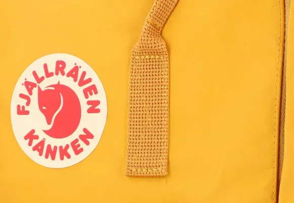 Primer plano del logotipo y la correa de una mochila Kanken amarilla